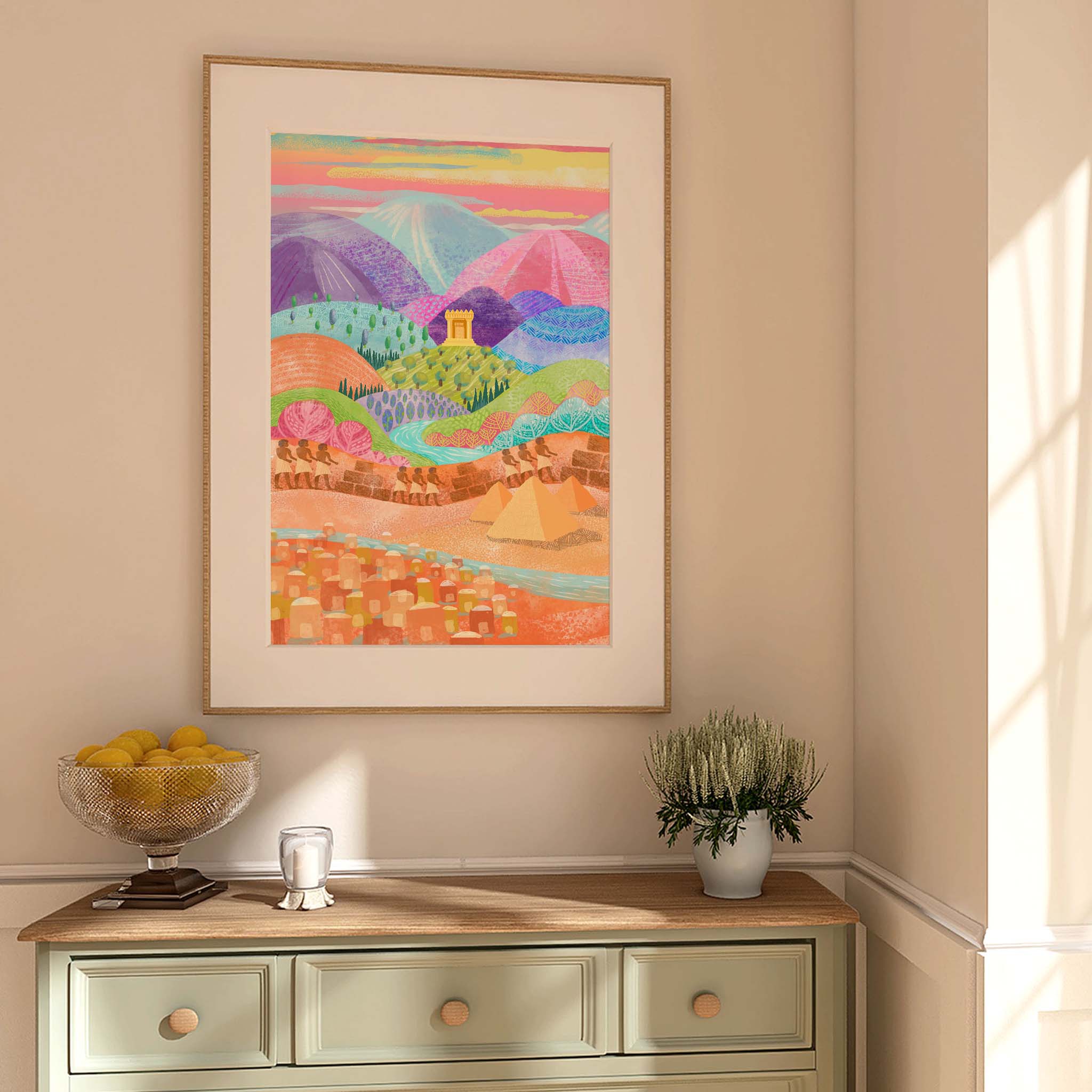 A framed colorful landscape art print of the life of the Hebrews in Egypt before the   Passover Exodus. The print features a vibrant, stylized countryside scene with hills, mountains, and a small house in pastel and bright hues.